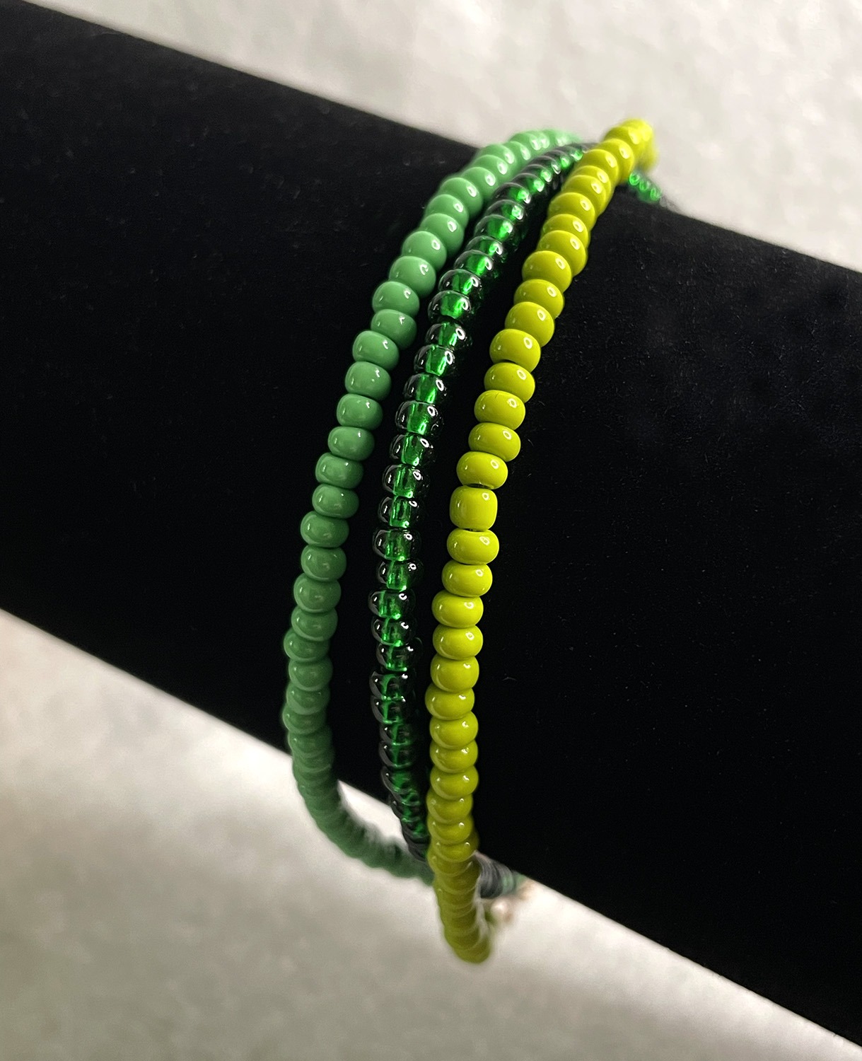 Three colorful beaded bracelets (green and yellow) wrapped around a wrist on a black background, shining beads visible.