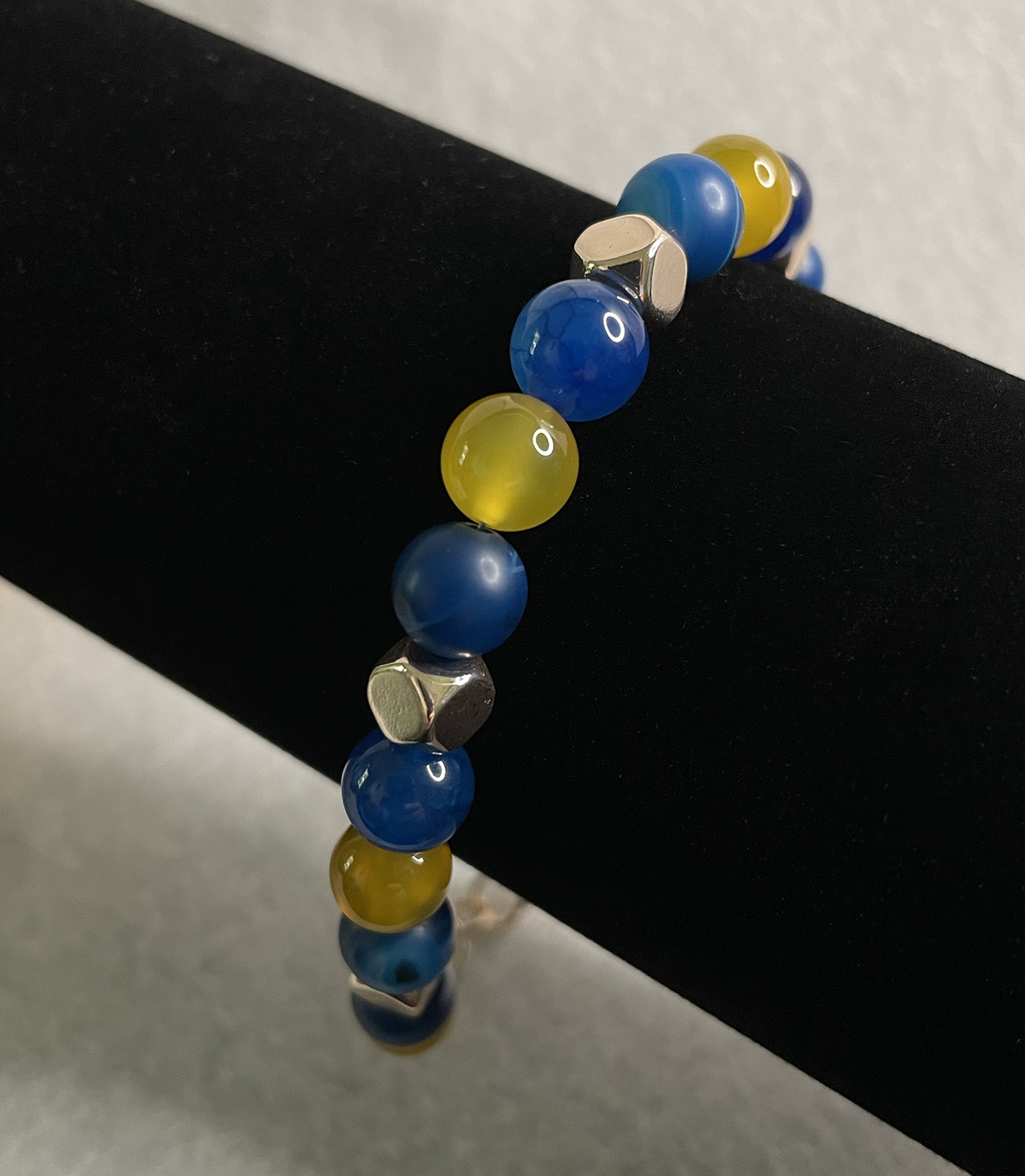 Beaded bracelet with blue and yellow glass beads and silver spacers on a black display stand.